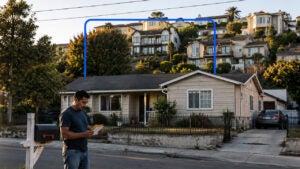 Man looks at mail with a home in the background and mansions on the hill beyond