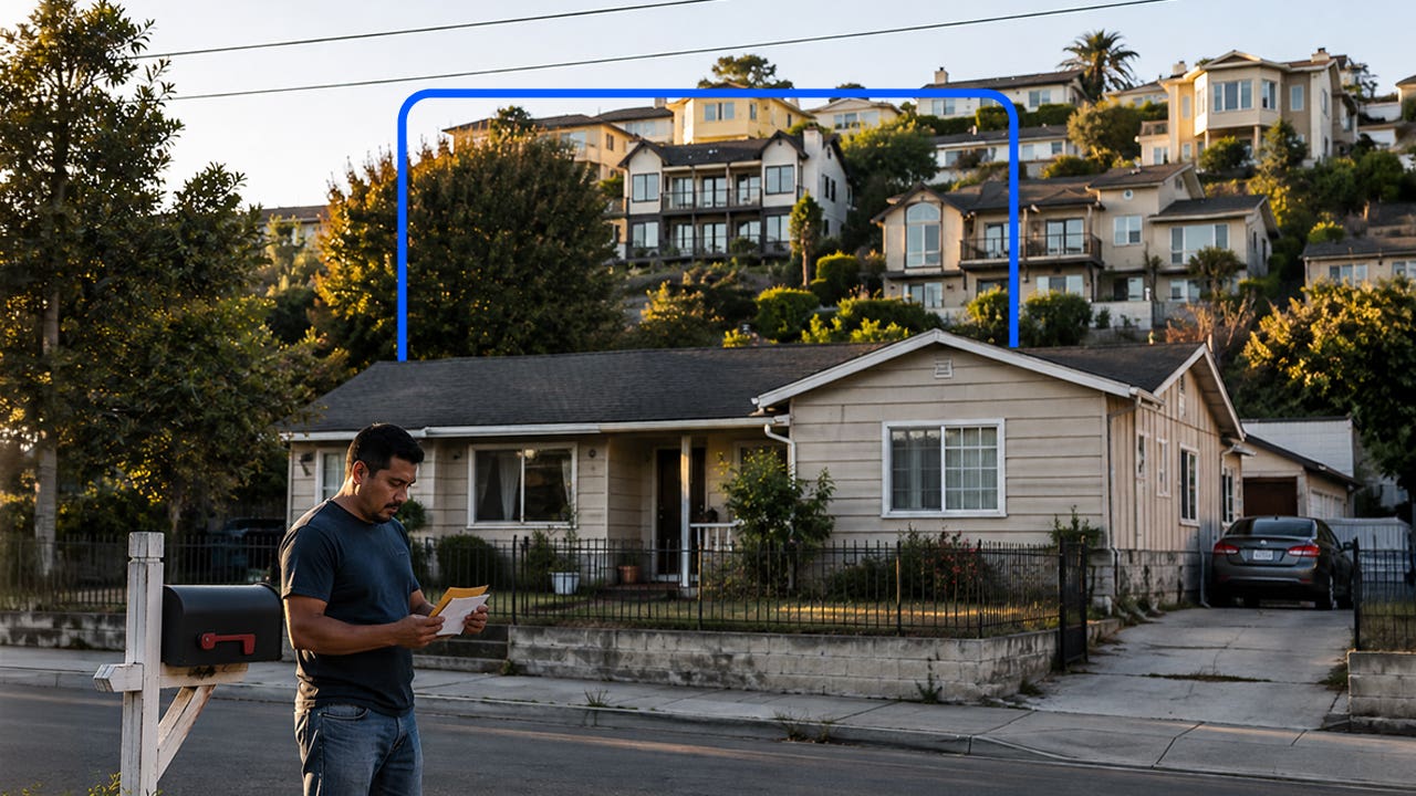 Man looks at mail with a home in the background and mansions on the hill beyond